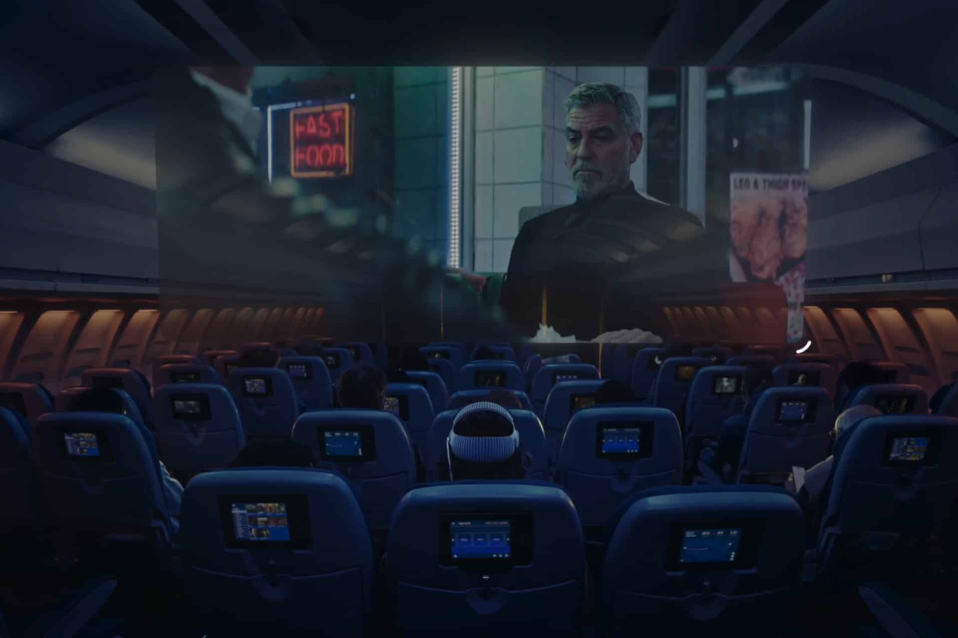 Passengers watch a movie on a large screen at the front of an airplane cabin, with individual seat-back screens visible and dim blue lighting throughout the interior—a glimpse into in-flight entertainment in the Spatial Computing Era.
