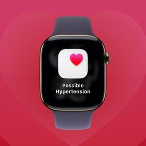 A smartwatch with a heart icon and the message "Possible Hypertension" on its screen, set against a red background with a faint heart shape and the Apple logo in the corner, highlights Preventive Heart Care features like tracking afib symptoms. - atrial fibrillation
