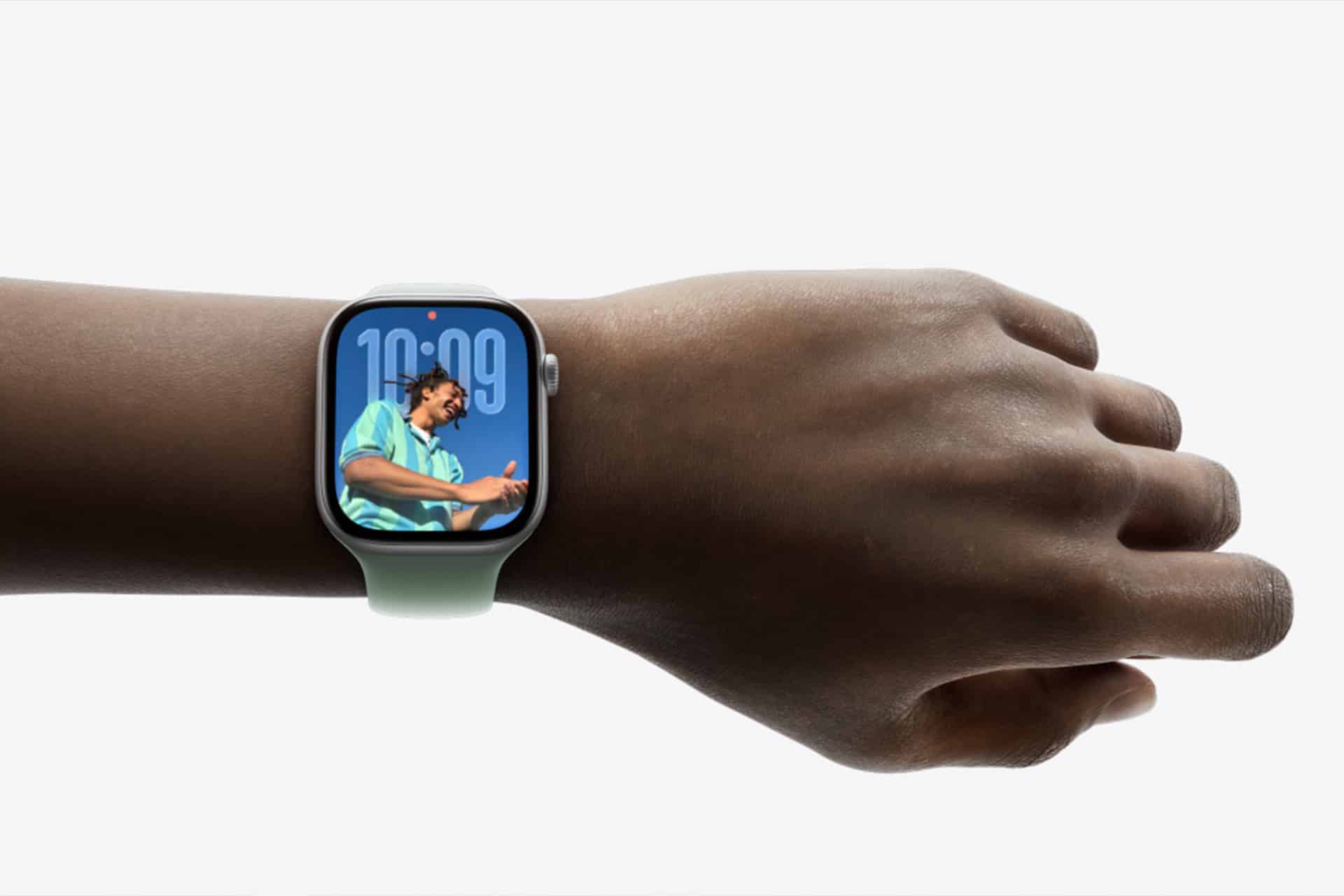 A hand wearing an Apple Watch with a light-colored band. The display shows "10:09" and features a large portrait of a person in a blue-green shirt, highlighting the convenience of Apple Watch Gestures.