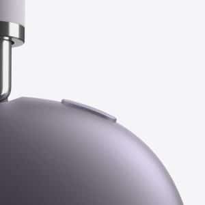 Close-up of a metallic charging cable being inserted into the top of a smooth, rounded, purple-gray device with a small button on its surface, set against a plain light background.