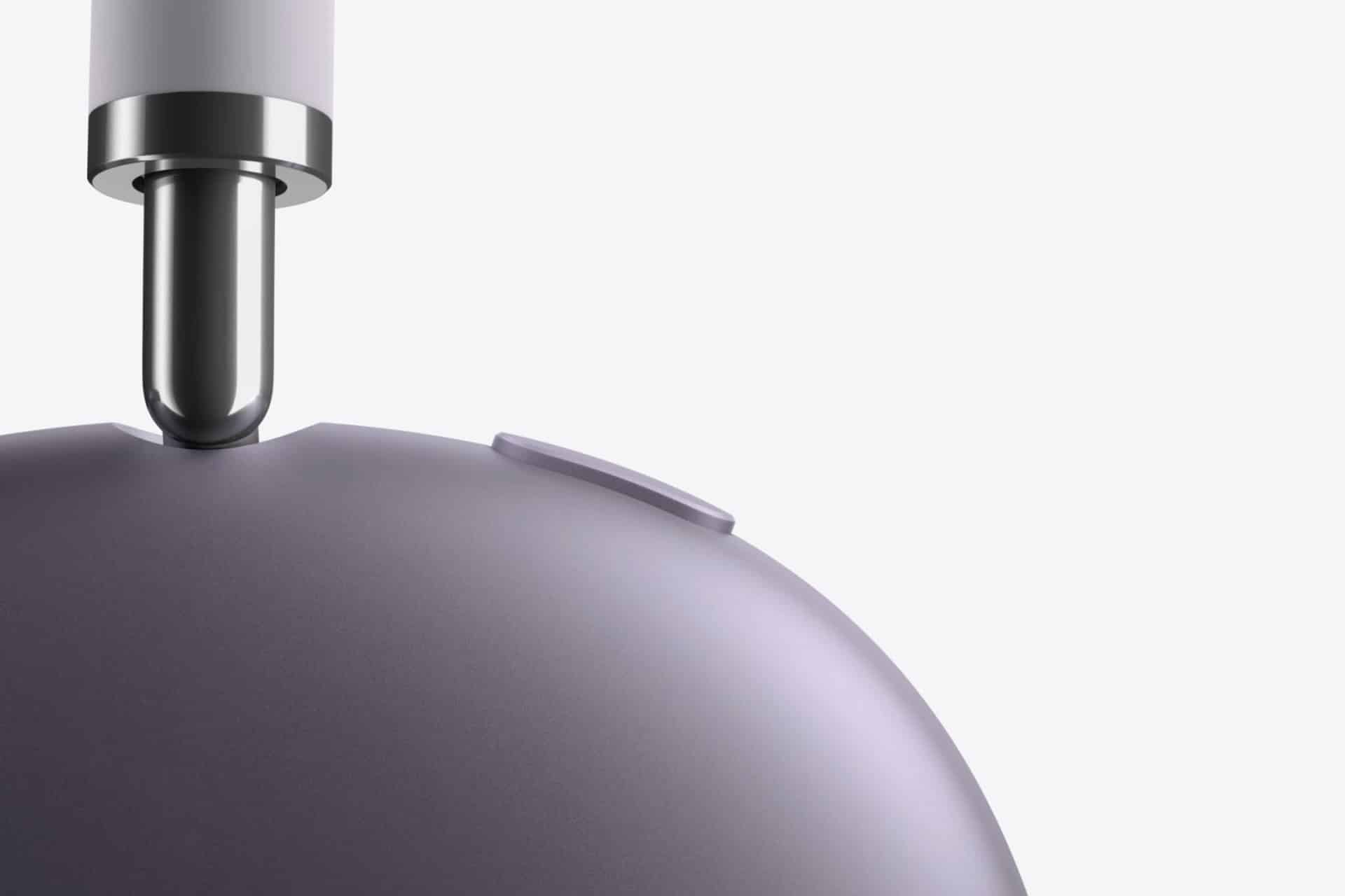 Close-up of a metallic charging cable being inserted into the top of a smooth, rounded, purple-gray device with a small button on its surface, set against a plain light background.