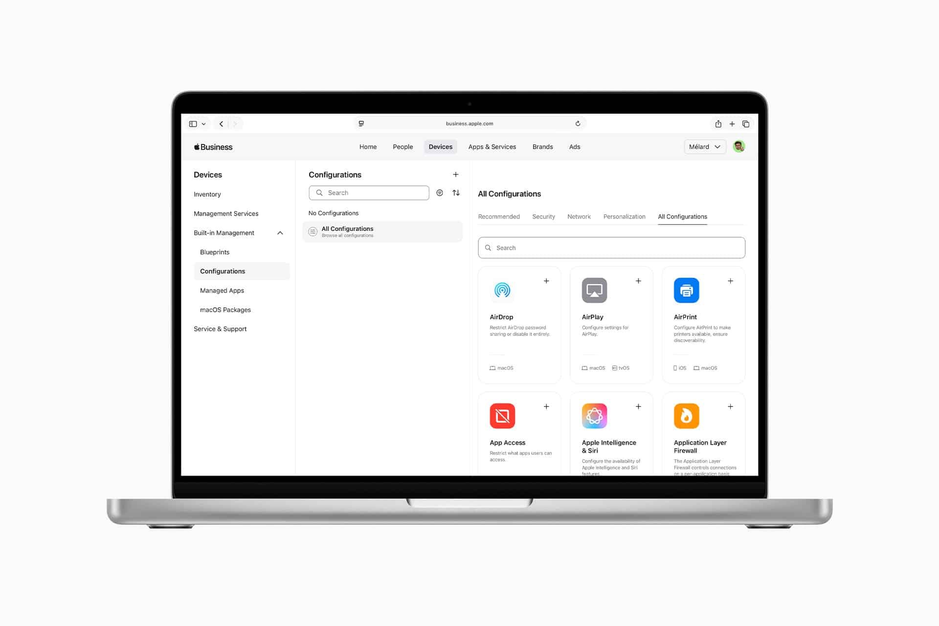 A laptop displays an Apple Business device management dashboard with a list of settings on the left and configuration options such as AirDrop, AirPlay, and App Store shown on the main screen.