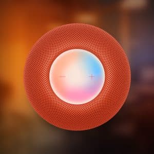 A close-up of a red Apple HomePod Mini smart speaker viewed from above, showing its mesh exterior and touch-sensitive top with minus and plus symbols—perfect for exploring Hidden Siri Commands—set against a blurred background.
