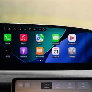 A Lucid Gravity CarPlay dashboard display shows various app icons—Phone, Music, Maps, Messages, Now Playing, Podcasts, Audiobooks, Calendar, and Settings—with a digital clock and route information conveniently on the side.