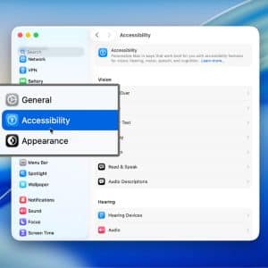 A computer screen shows the Accessibility settings menu open, with a dropdown highlighting “Accessibility” between “General” and “Appearance.” The menu includes options like MacBook Screen Zoom, with a cursor pointing at the selection.