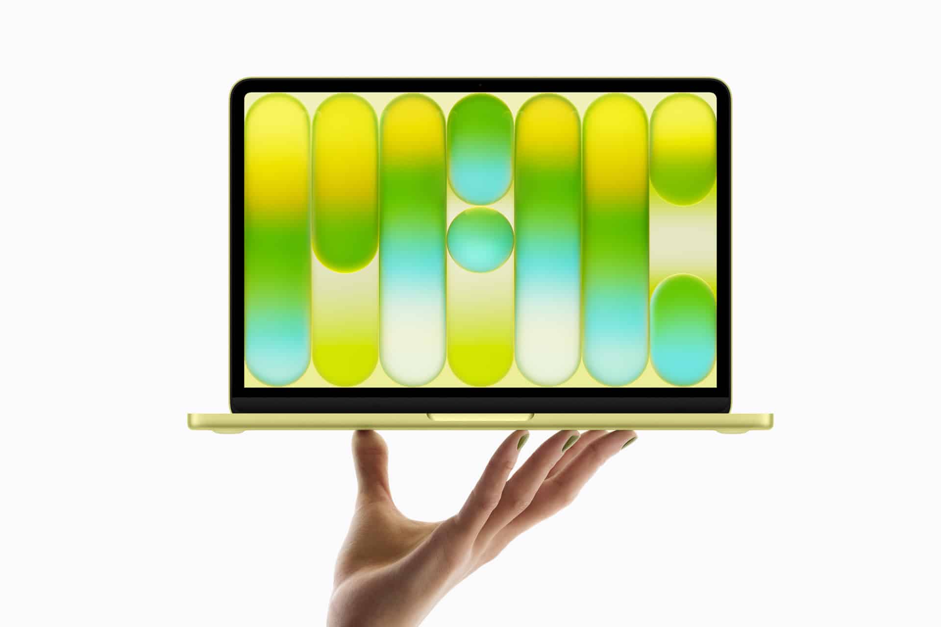 A hand holds up a thin, yellow laptop with a colorful abstract pattern of green, yellow, and blue shapes displayed on its screen against a white background.