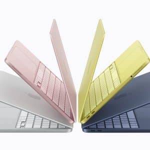 Four Apple MacBook Air laptops in silver, pink, yellow, and blue are arranged in a fan shape, partially open with screens facing outward, showcasing their colorful exteriors and slim designs.
