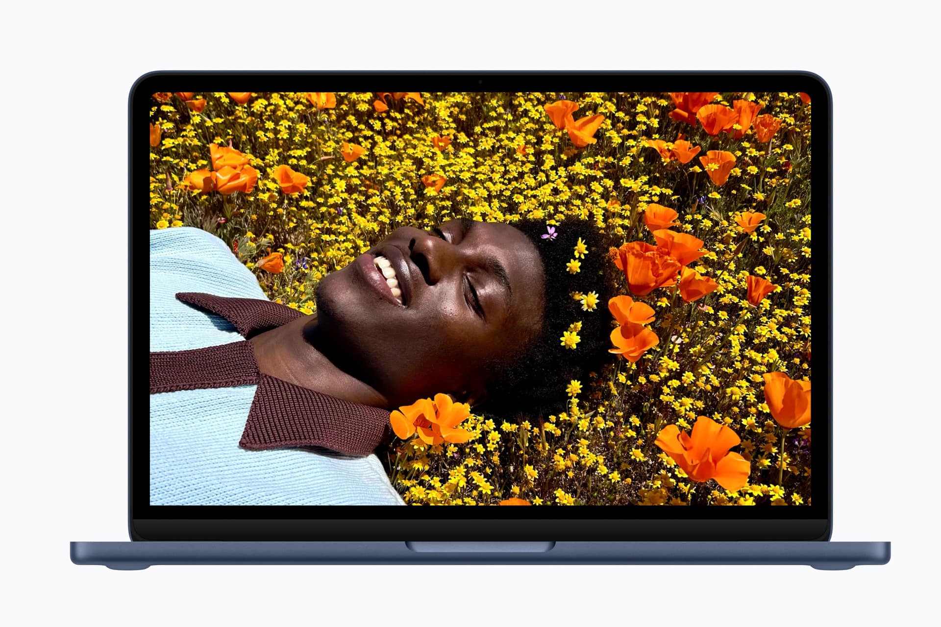 MacBook Neo - A laptop screen displays a vibrant image of a person lying in a field of yellow and orange flowers, smiling and looking relaxed. The flowers surround their head, creating a colorful, cheerful scene.