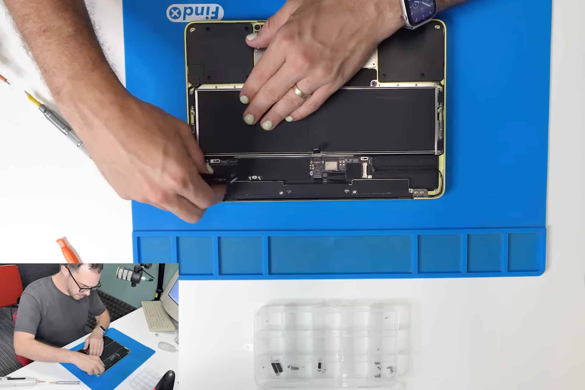 Person with painted nails uses a tool to work on an open MacBook Neo Repair on a blue mat, with a parts tray nearby. Inset shows the same person at a desk, assembling or repairing the MacBook.