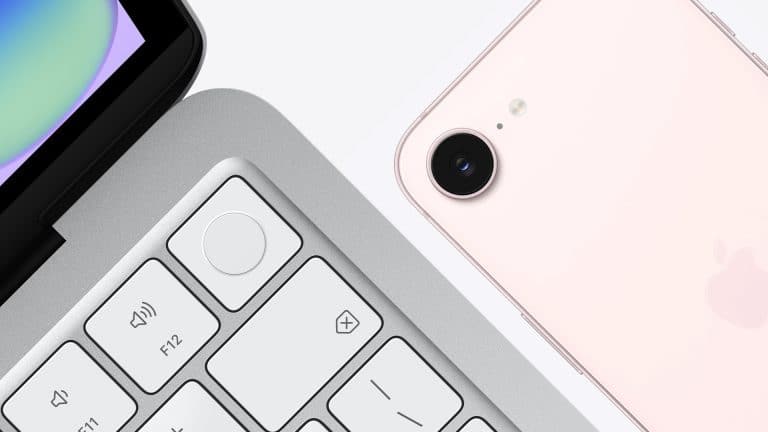 Close-up of a silver laptop keyboard beside the back of a light pink smartphone with camera lens and flash, both on a white surface—an everyday scene reflecting the subtle impact of Apple ecosystem lock in.