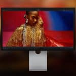 A widescreen Studio Display XDR showcases a vibrant portrait of a woman in a gold fringed outfit against a colorful background, with the Apple logo visible in the lower right corner.