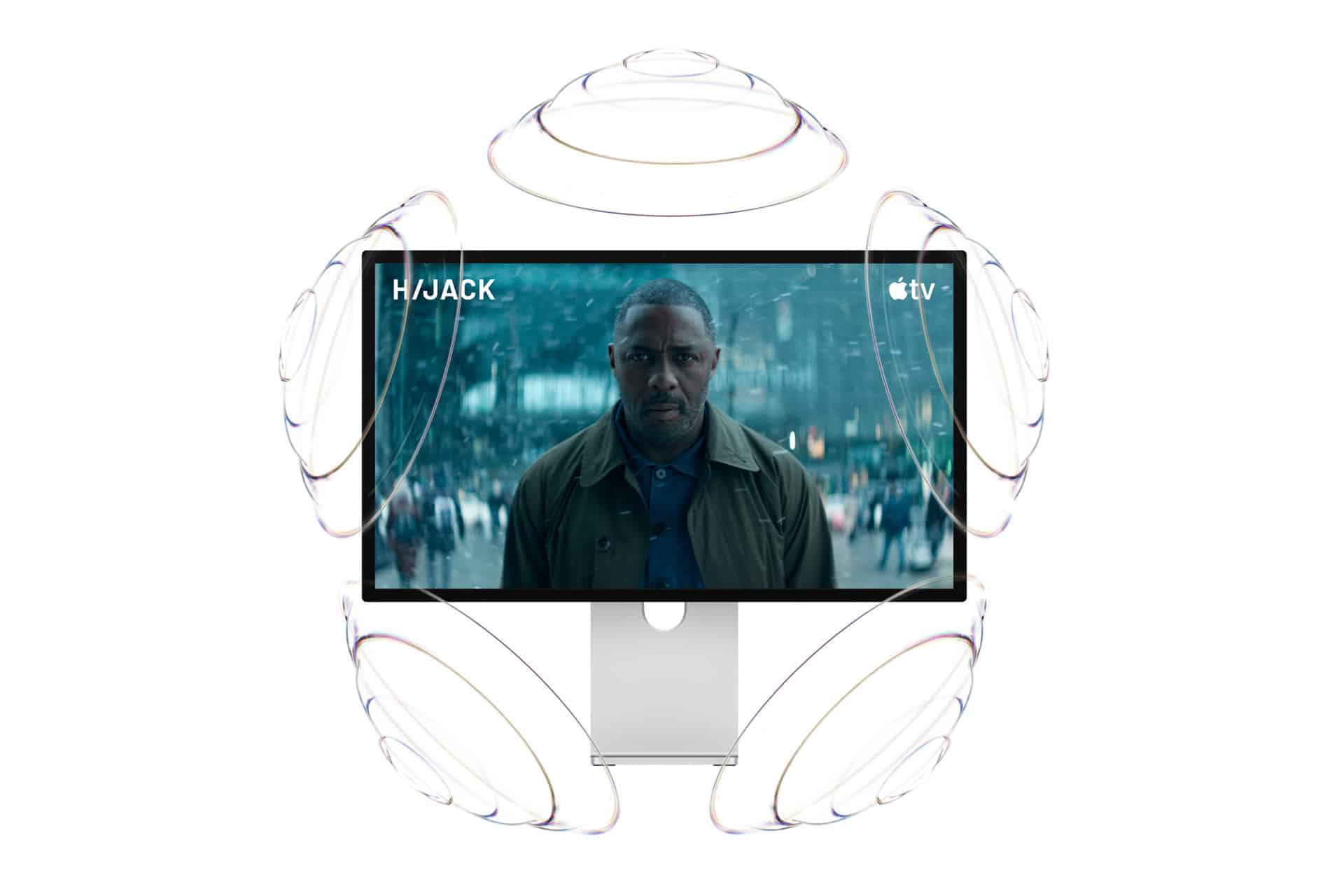 A Studio Display XDR shows a scene from "Hijack" on Apple TV+, with a serious-looking man in a crowd. Circular soundwave graphics surround the monitor, illustrating immersive audio.