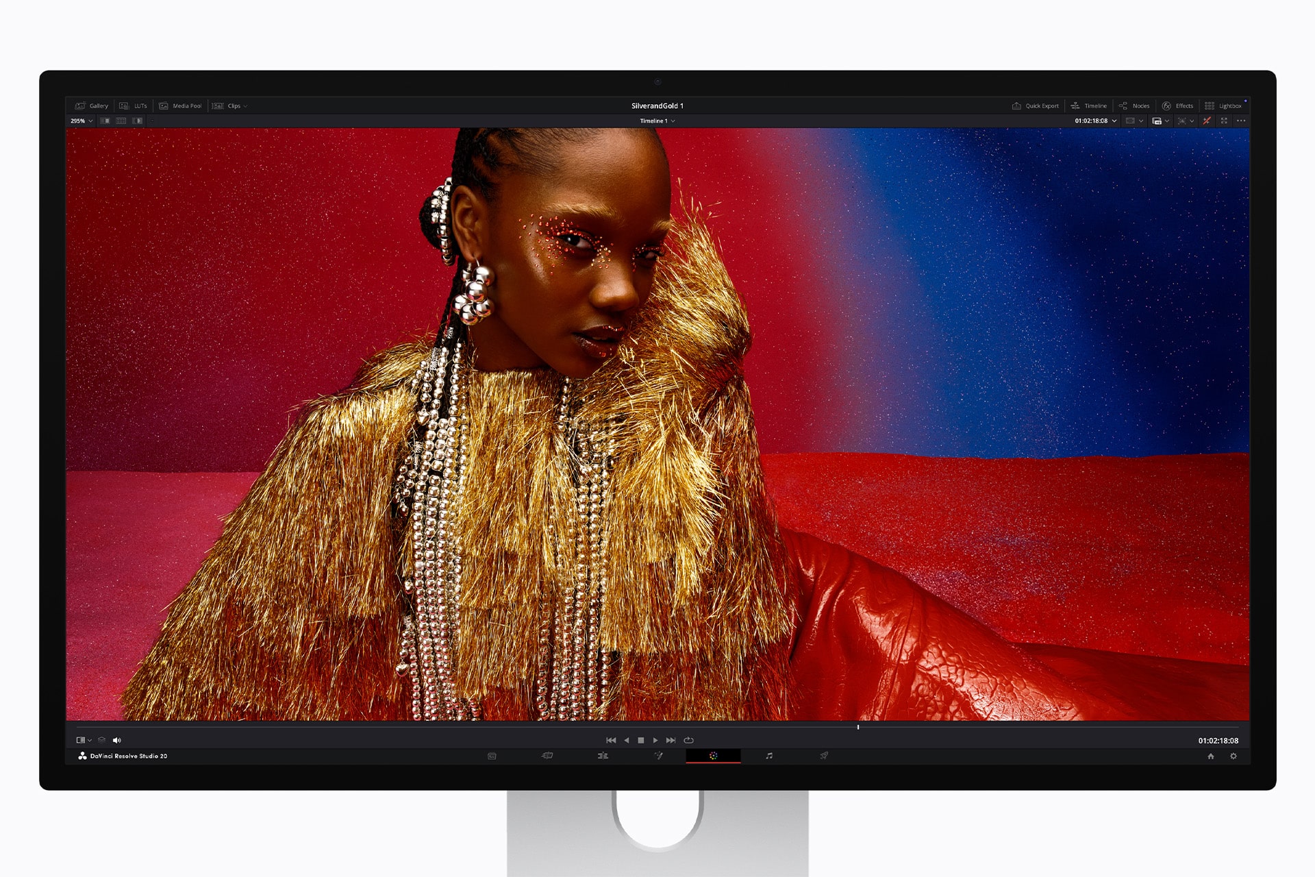 Studio Display XDR - A computer monitor displays a vibrant photo of a woman wearing gold fringe and pearl accessories, set against a colorful red and blue background with sparkly eye makeup.