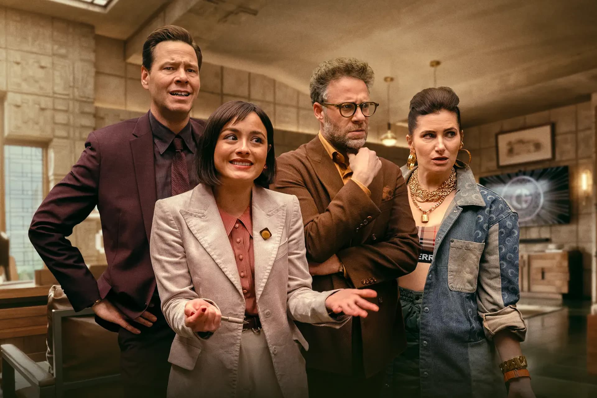 Four people stand together indoors, dressed in stylish, modern outfits, appearing engaged and expressive in an office or detective agency setting—possibly a scene from Apple TV The Studio, with beige walls and a desk in the background.