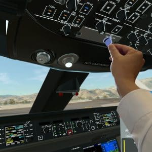 A person in a cockpit interacts with overhead controls in an airplane, using X-Plane Vision Pro. The view shows a hand reaching up to switch a knob, with aircraft instruments, runway, mountains, and another plane visible outside.