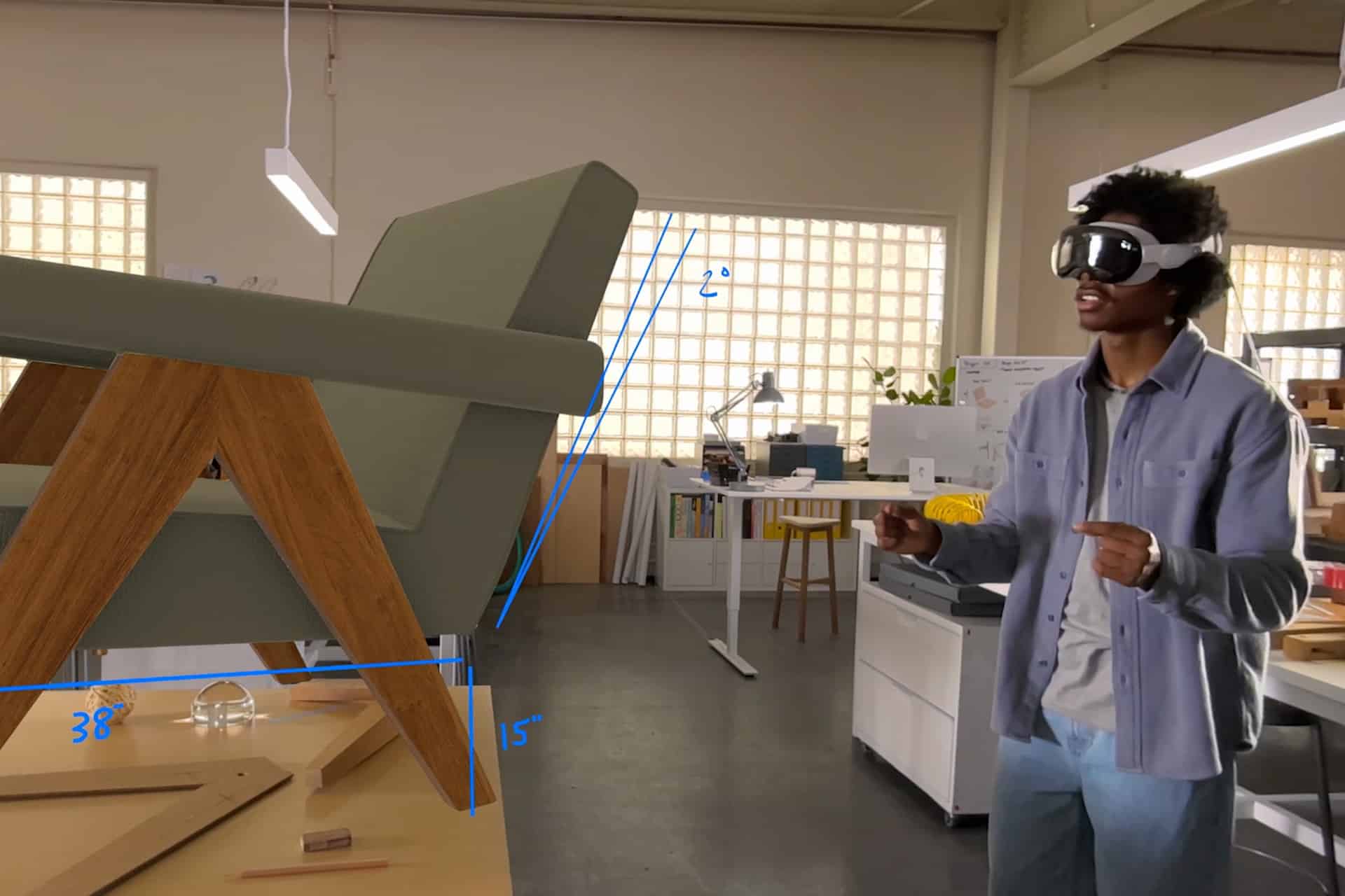 A person wearing a VR headset stands in an office, using Vision Pro Gestures to interact with a large, virtual 3D model of a chair. Blue lines and measurements (38", 15", 42") highlight the chair's dimensions.
