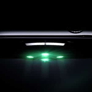 A close-up, low-light image of the underside of a smartwatch emitting green light from its sensors, highlighting its sleek metallic finish and side buttons, showcases the watch’s focus on oxygen accuracy.