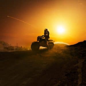 A person wearing a spacesuit rides an ATV on a rocky, barren landscape at sunset, beneath the orange sky of For All Mankind. A streak from a meteor or rocket arcs across the backdrop, highlighted by the setting sun.