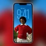 A smartphone displays its lock screen with a smiling person in a red sweater and white shirt as the wallpaper. The time reads 9:41, and there are calendar and notification icons visible. The Apple logo is in the bottom right corner.