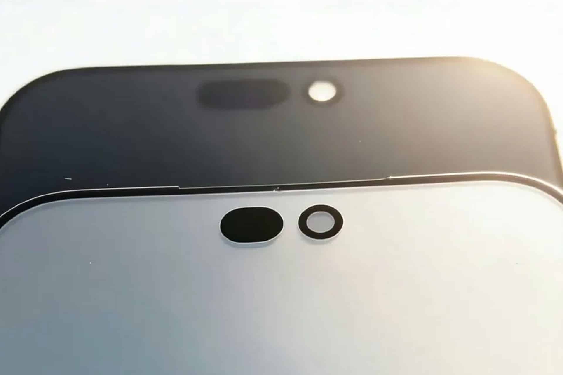 Close-up of two smartphone screens, one black and one white, each showing front camera cutouts and sensor holes, possibly hinting at a Dynamic Island design. Bright light is visible in the background in these first images from an iPhone 18 leak.