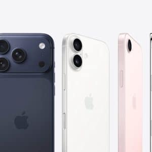 Four Apple iPhones in different colors—dark blue, white, pink, and silver—are shown from the back and side, highlighting their camera designs and sleek edges against a light background, alongside the Apple Watch Find Devices feature.