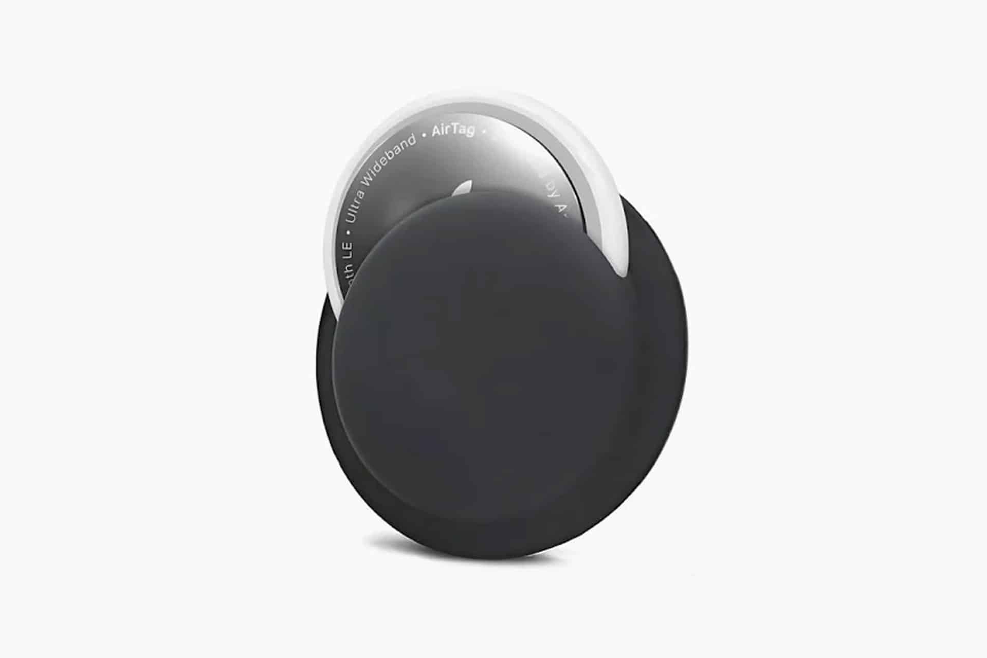 A black circular case, one of many AirTag accessory choices, partially covers a white Apple AirTag device, both set against a plain white background.