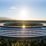 The image shows a large, circular modern building surrounded by trees, with the sun rising or setting in the background. The sleek, white architecture resembles Apple’s campus—an icon often seen in discussions about their Q2 earnings.