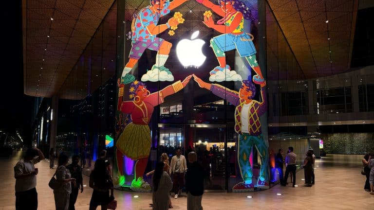 People stand outside an Apple Store at night, vibrant mural and glowing logo above them. The lively scene hints at more than tech—Apple’s success reflects a smart cash reserve strategy behind the colorful, bustling storefront. India Store.