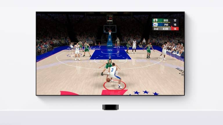 A TV mounted on a white wall shows a basketball video game as part of an Apple TV gaming setup, with a player in white dribbling toward the basket against green and the scoreboard reading BOS 12, PHI 16, 2nd quarter, 4:48 left.