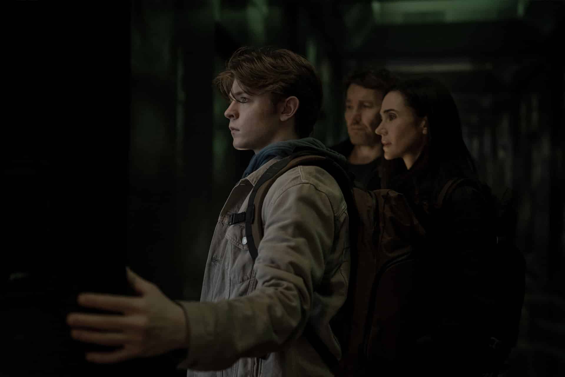 A young man with outstretched arm stands in a dimly lit hallway, while two adults watch him closely from behind. All three appear focused and tense, capturing the suspenseful atmosphere of the Dark Matter Series.