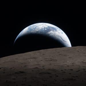 A view of Earth rising above the Moon’s rough, gray surface, a crescent illuminated and most in shadow, set against the blackness of space—captured with detail as sharp as Apple GPU memory enables.