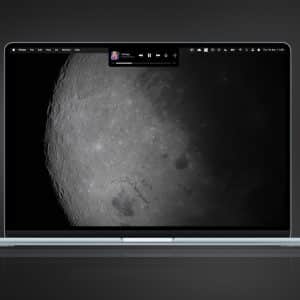 A MacBook displays a close-up photo of the moon's surface as its wallpaper, with a small music player widget at the top center. The minimalist dark gray background adds to the Magic Island feel of this celestial workspace.