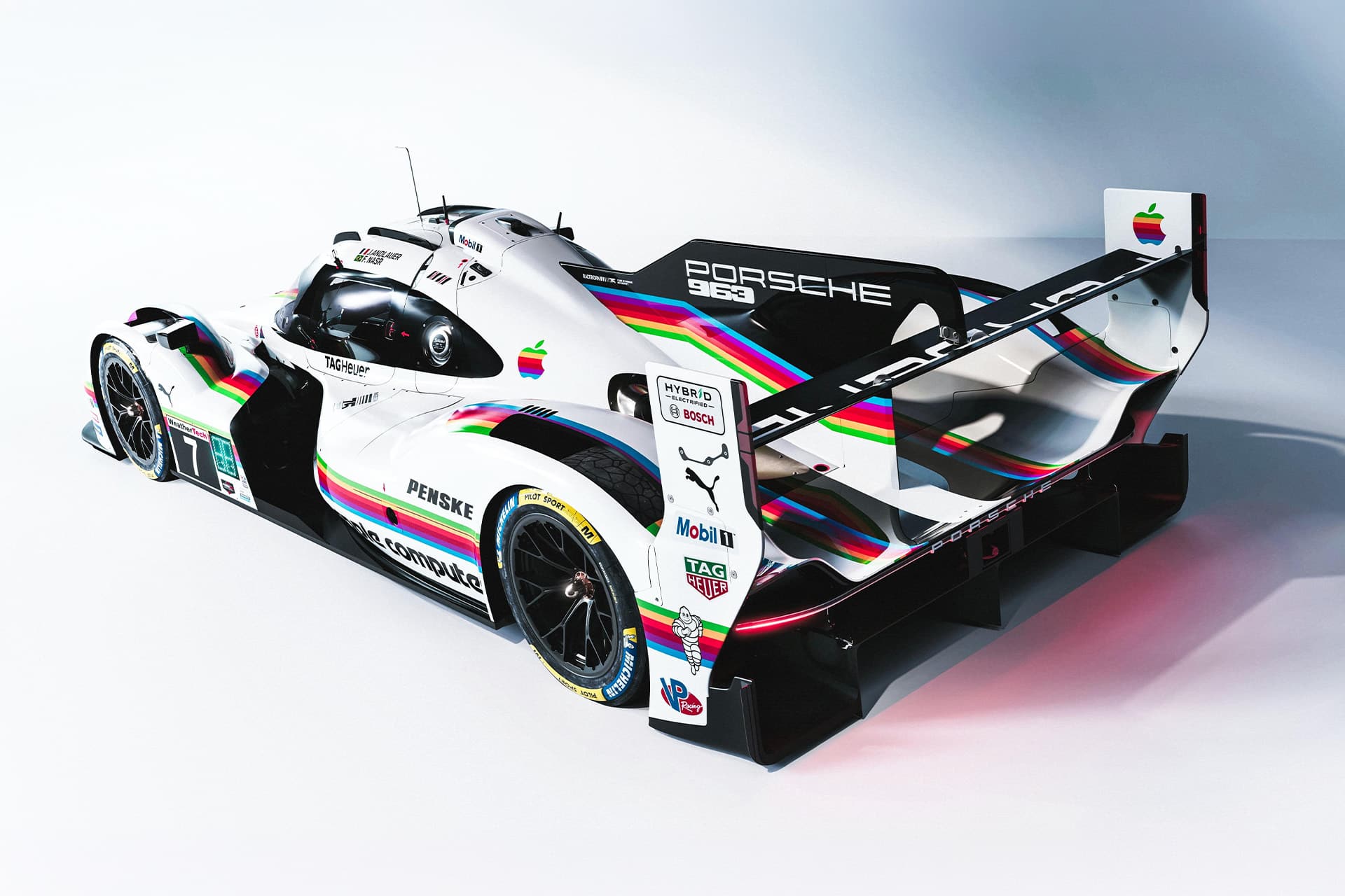 A white Porsche Apple race car with rainbow stripes and retro Apple logos on the rear wing and sides, displayed in a well-lit studio with a clean, neutral background.