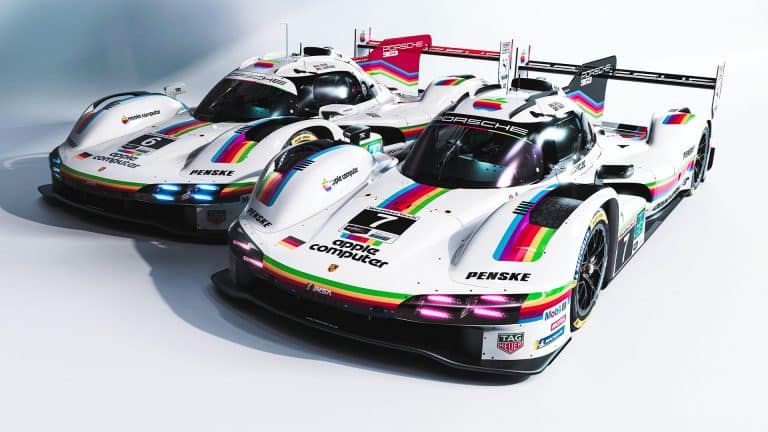 Two white Porsche Apple race cars with rainbow stripes and retro “Apple Computer” logos are parked side by side in a studio setting, proudly displaying racing numbers and various sponsor logos on their sleek bodies.