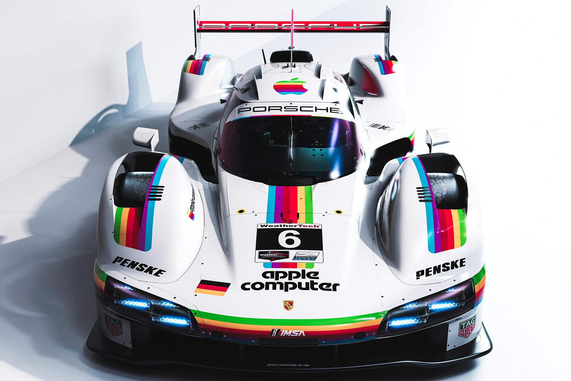 A Porsche Apple race car with colorful retro Apple stripes, a large Apple logo on the hood, "apple computer" text, and #6. The car features prominent Porsche branding, Penske logos, and striking aerodynamic design details.