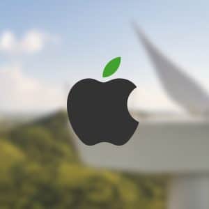 The black Apple logo with a green leaf is centered over a blurred background of a wind turbine and green hills, symbolizing Apple sustainability partners' commitment to renewable energy and environmental sustainability.