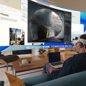 A man wearing a VR headset sits on a couch with a laptop, using Vision Pro Mac Display to view multiple large virtual screens showcasing travel and nature content in a modern living room.
