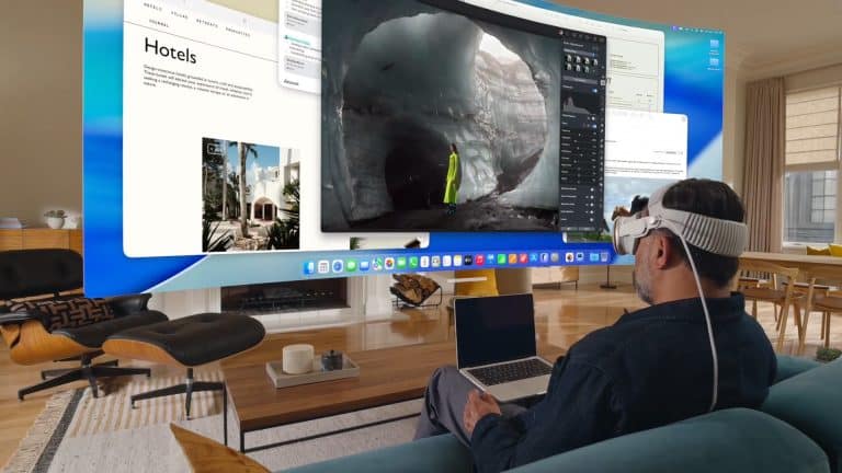 A man wearing a VR headset sits on a couch with a laptop, using Vision Pro Mac Display to view multiple large virtual screens showcasing travel and nature content in a modern living room.
