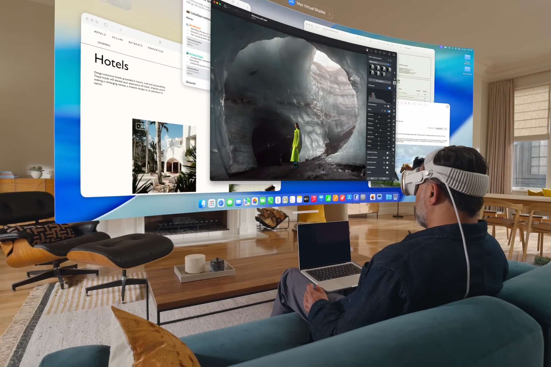 A man wearing a VR headset sits on a couch with a laptop, using Vision Pro Mac Display to view multiple large virtual screens showcasing travel and nature content in a modern living room.