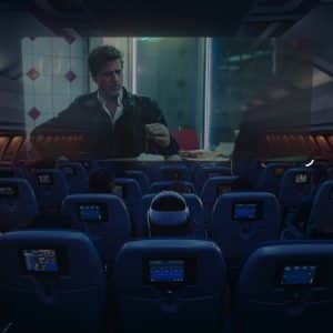 Passengers watch a movie on a large screen at the front of a dimly lit airplane cabin, with individual seatback screens and the option to use Apple Vision Pro travel mode for an immersive in-flight entertainment experience.