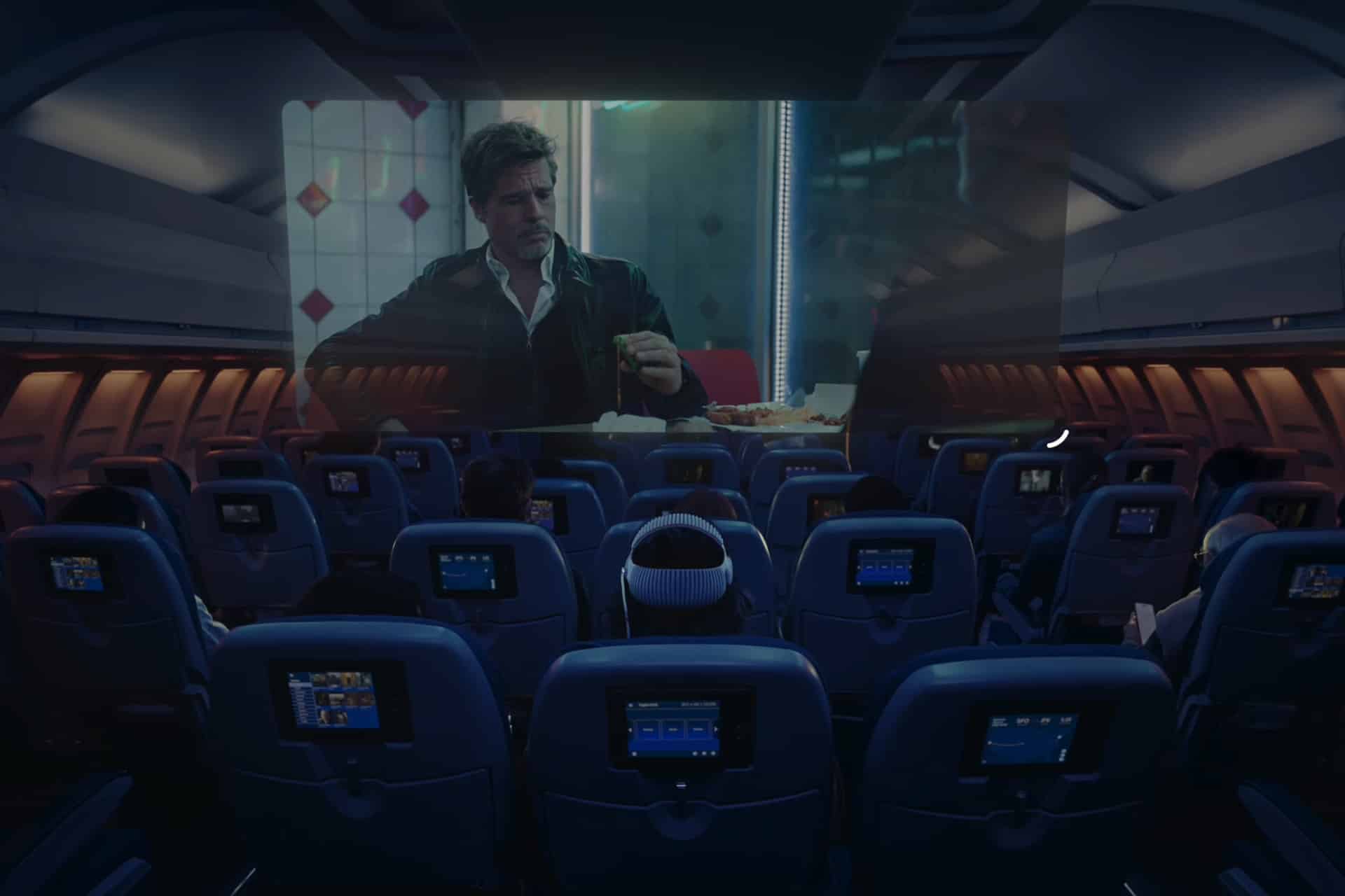 Passengers watch a movie on a large screen at the front of a dimly lit airplane cabin, with individual seatback screens and the option to use Apple Vision Pro travel mode for an immersive in-flight entertainment experience.