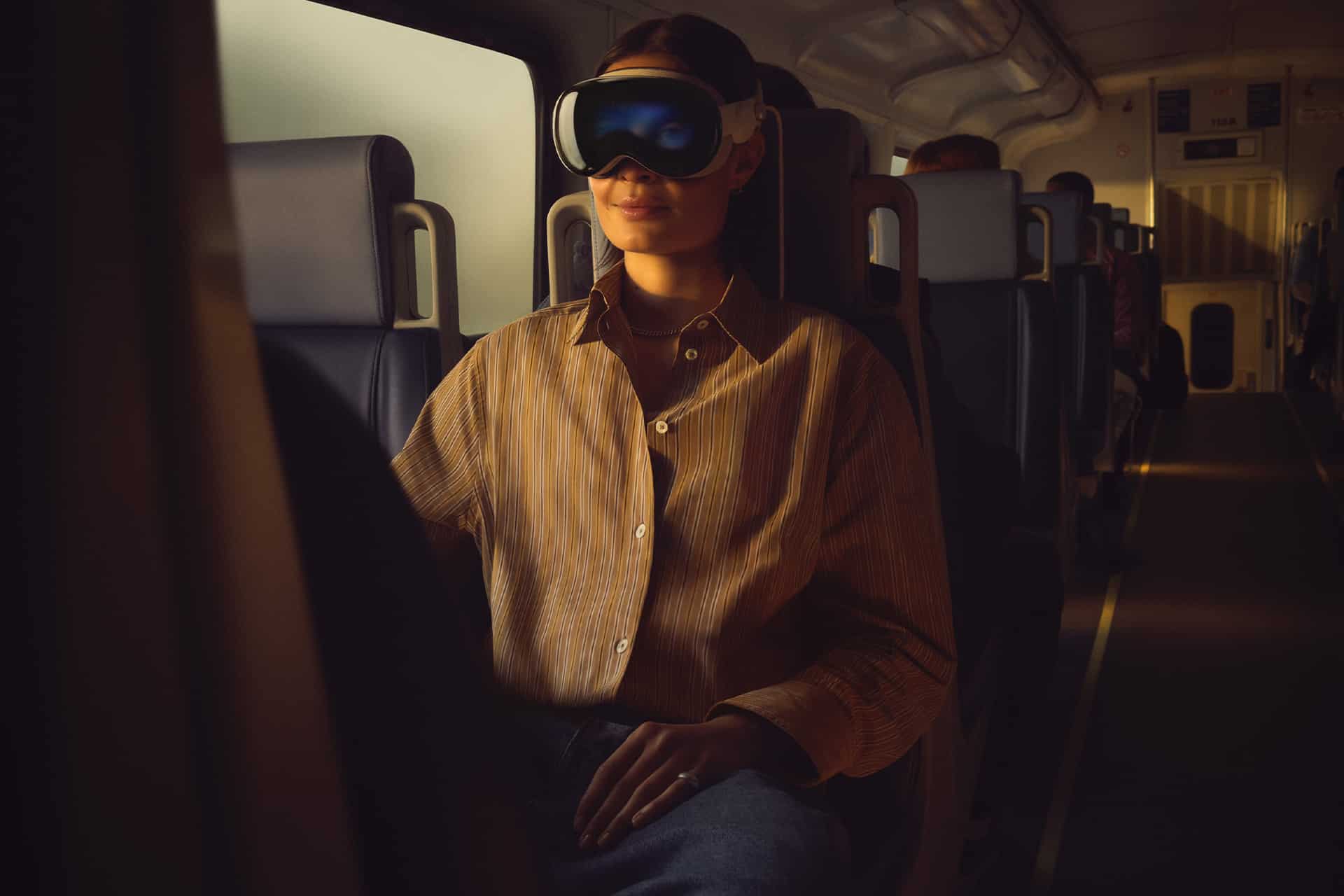 A person wearing an Apple Vision Pro headset sits calmly on a train, bathed in warm light with empty seats around them, enjoying travel mode for a serene journey.