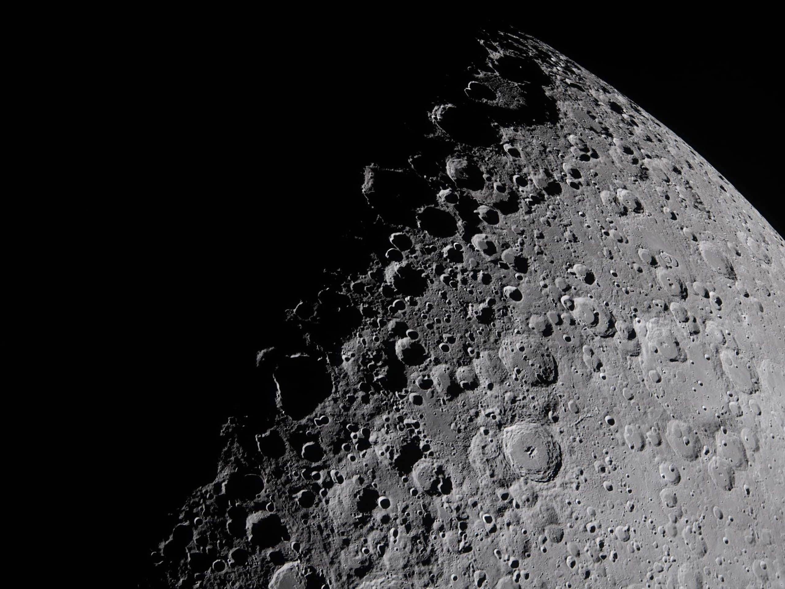 A detailed close-up of the moon’s surface, showing numerous craters and rough terrain—rendered with clarity akin to Apple GPU memory—under stark lighting, with deep shadows emphasizing the lunar landscape against a black background.