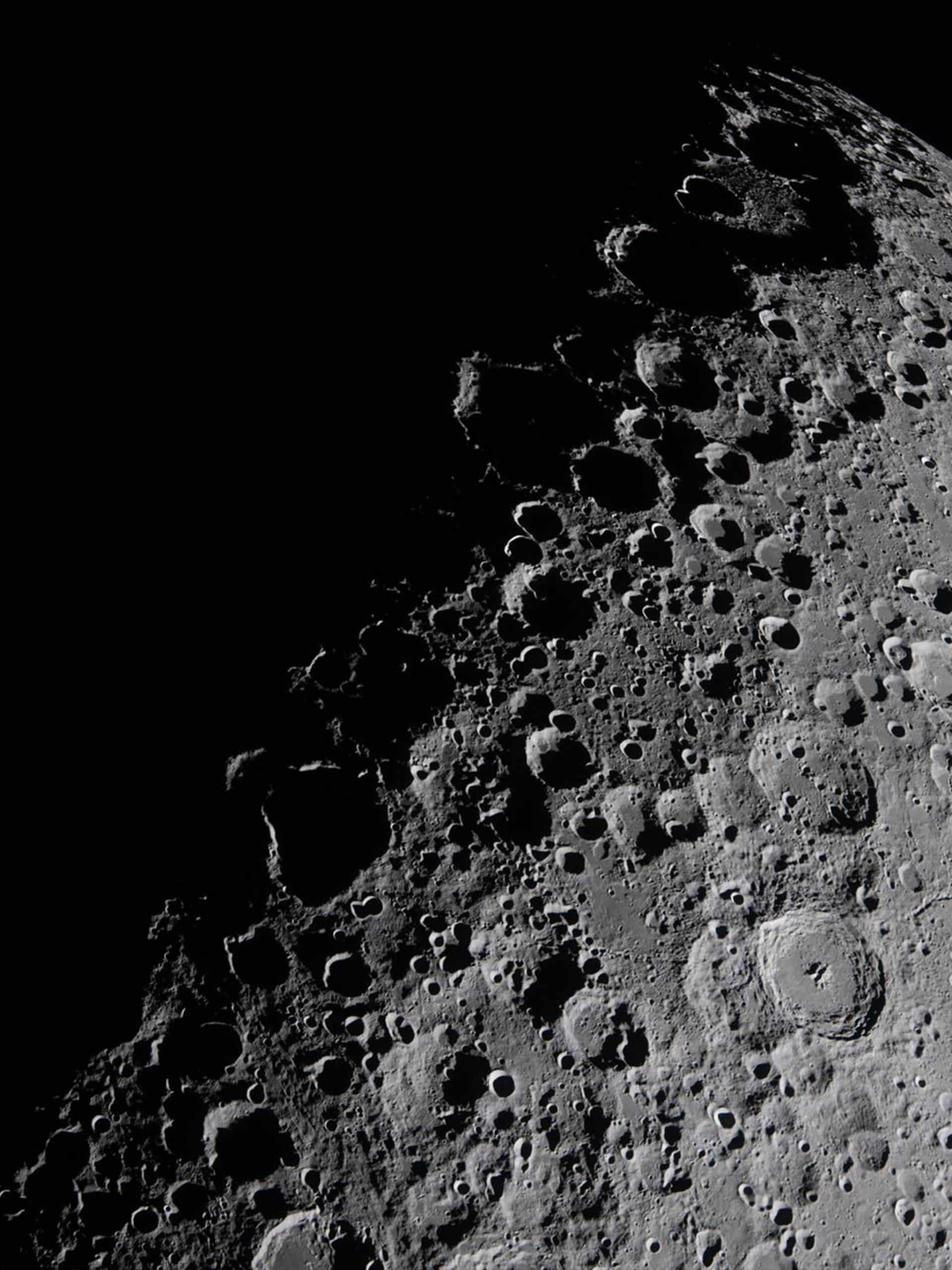 A high-resolution image shows a rugged, cratered surface of the Moon, with deep shadows accentuating the texture—beautifully rendered as if by Apple GPU memory. The lunar terrain is side-lit, with the blackness of space in the background.