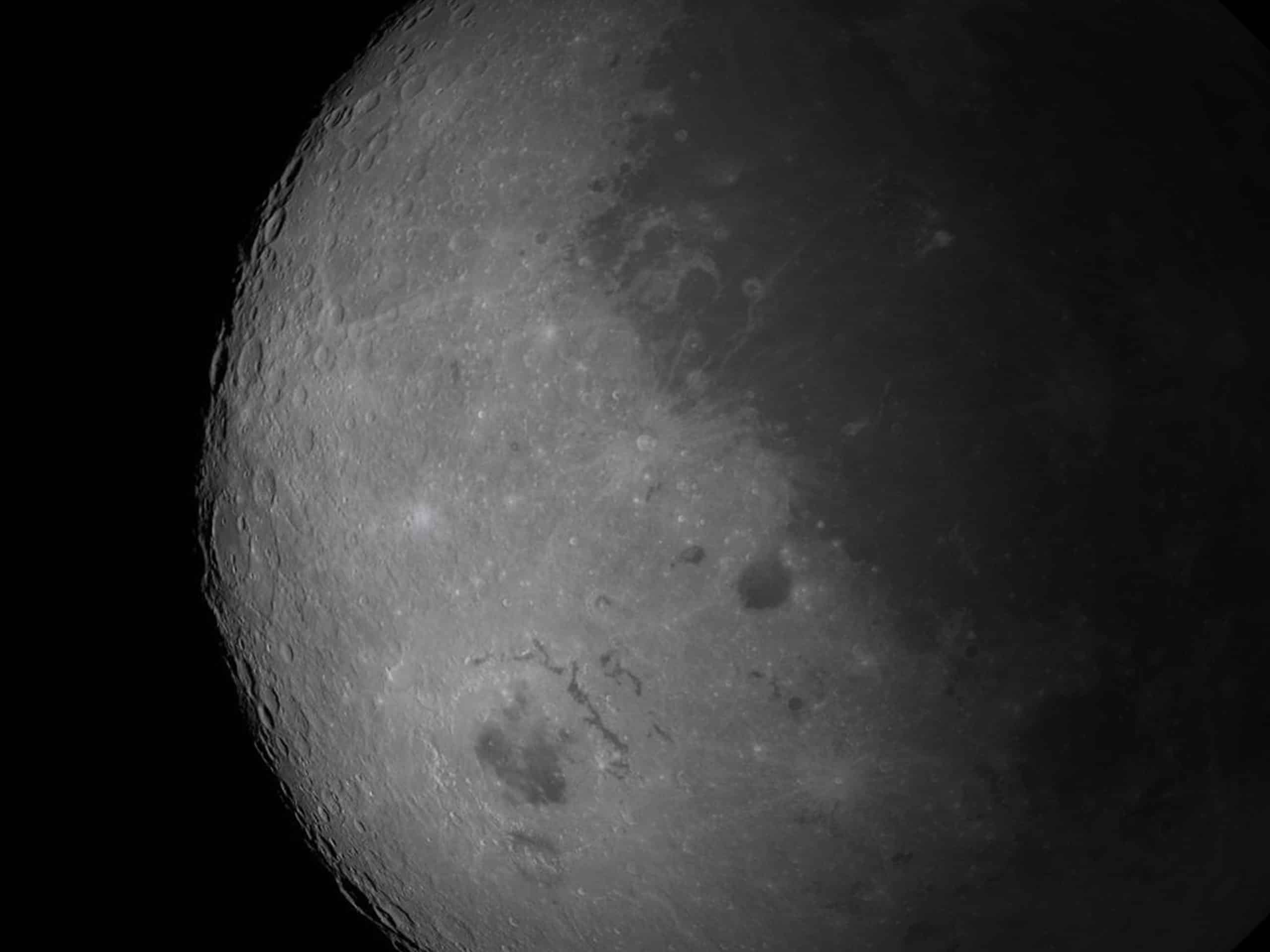 A close-up view of the Moon’s surface, showing numerous craters and rough terrain, as sharply rendered as if processed with Apple GPU memory, with one side brightly lit and the other in shadow against the blackness of space.