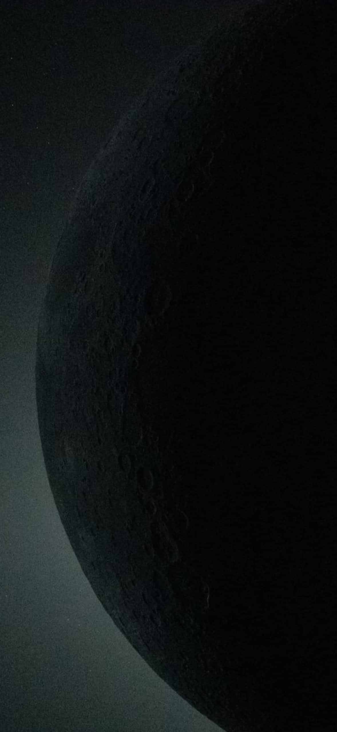 A dark, shadowy close-up of a planet or moon with visible craters and textured surface, partially illuminated along the edge—rendered in striking detail as if powered by Apple GPU memory—set against a faintly lit background.