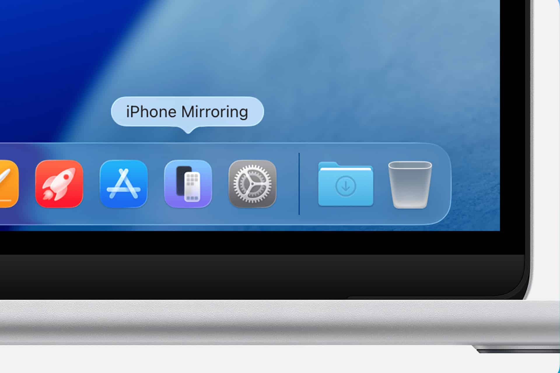 Close-up of a MacBook screen showing the dock with several app icons, including Settings, and a highlighted iPhone Mirroring feature above the dock. The edge of the silver laptop is visible.