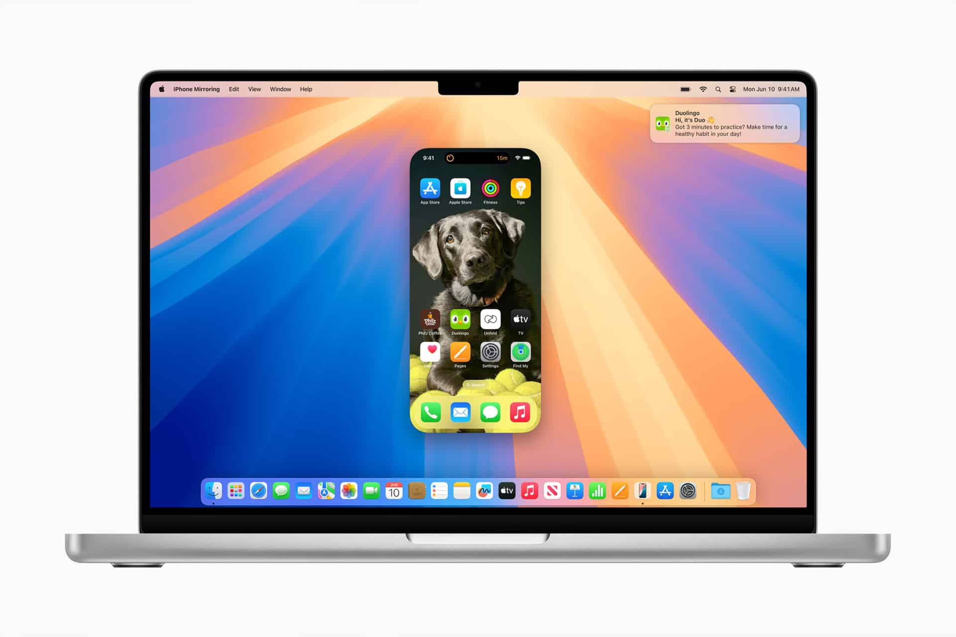 A MacBook displays the iPhone Mirroring feature, with a phone screen showing a playful dog wallpaper and app icons, set against a colorful, radiant background on the laptop.