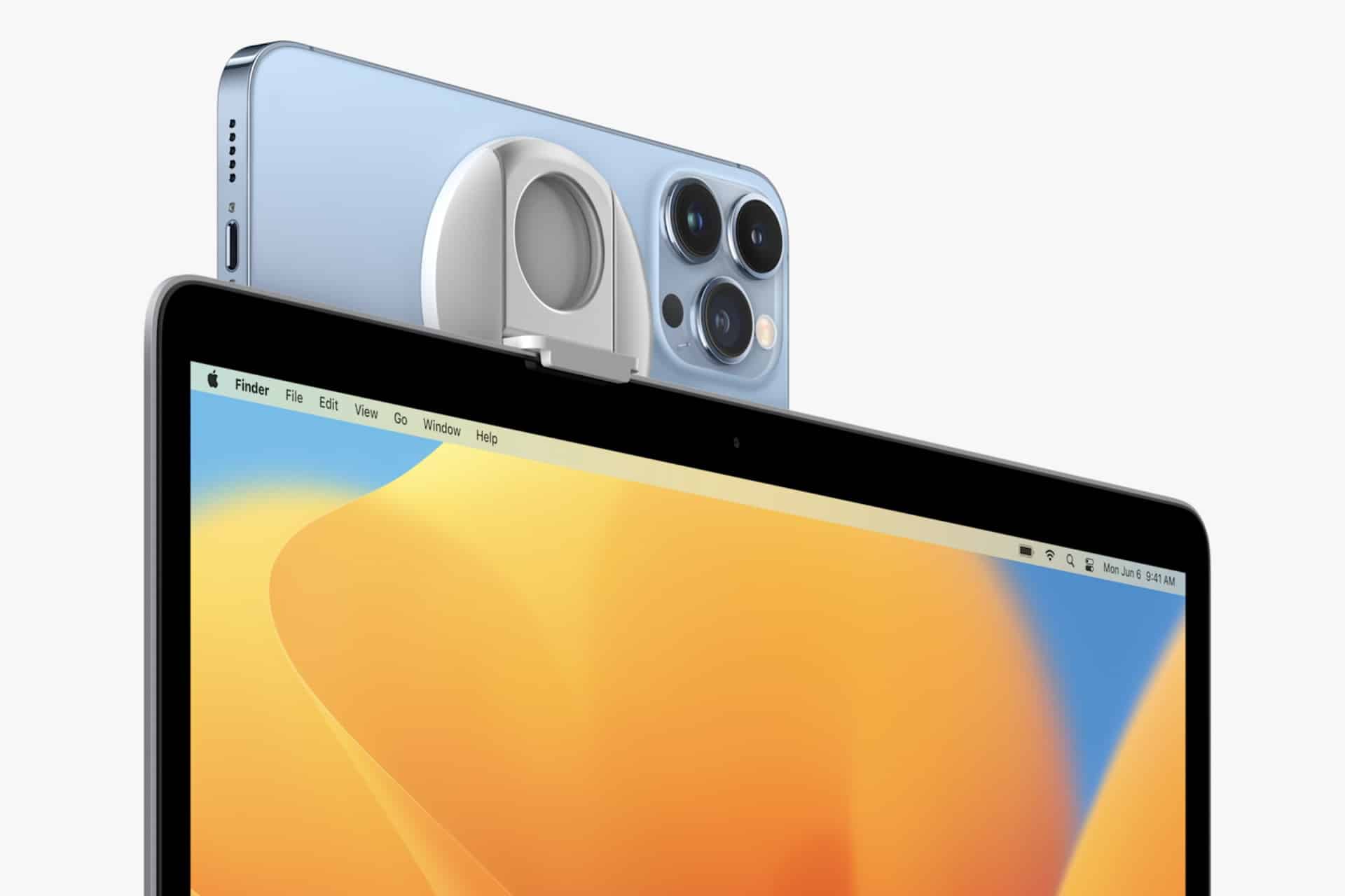 A blue iPhone with three cameras is mounted on top of a computer screen using a round, silver clip accessory, showcasing Mac Continuity Camera while the computer displays a desktop interface.