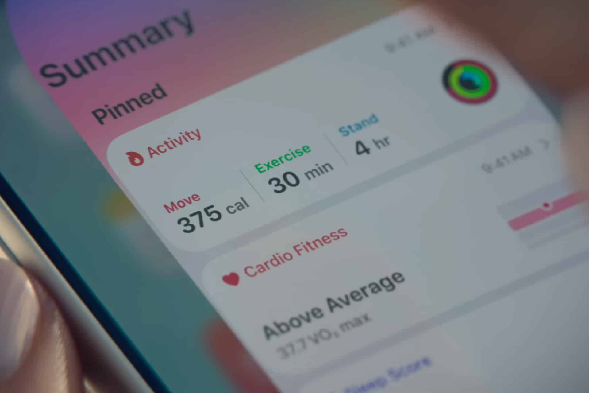 Close-up of a smartphone screen paired with Apple Health, displaying a fitness summary: 375 calories moved, 30 minutes of exercise, and 4 hours standing. Cardio fitness is labeled "Above Average" with a VO₂ max reading.